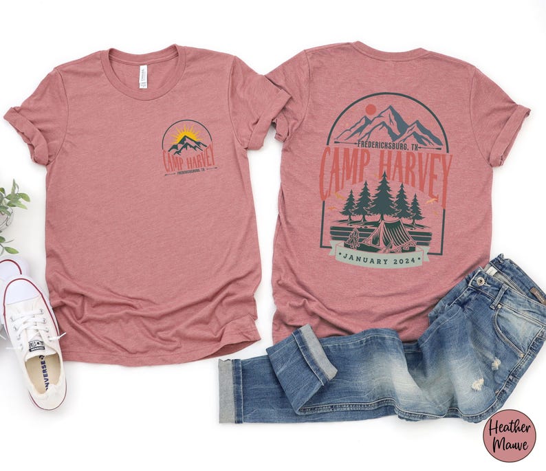 K&ouml;nnte beinhalten: Ein kurz&auml;rmeliges T-Shirt in Mauve-Melange mit einer kleinen Grafik auf der Vorderseite und einer gro&szlig;en Grafik auf der R&uuml;ckseite. Die Motive zeigen Berge, Tannen und ein Zelt mit dem Text Camp Harvey, Fredericksburg, TX, und January 2024 in Rot und Gr&uuml;n.