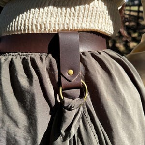 Puede incluir: Un cinturón de cuero marrón con un anillo de metal y una correa de cuero marrón. El cinturón se lleva alrededor de la cintura y la correa está unida al anillo.