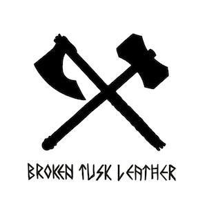 Puede incluir: Silueta negra de un hacha y un martillo cruzados. El hacha está a la izquierda y el martillo a la derecha. Debajo de las herramientas cruzadas está el texto "BROKEN TUSK LEATHER" en una fuente estilizada.