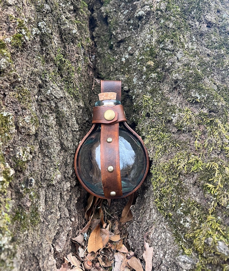 Puede incluir: Una botella redonda de vidrio con una envoltura de cuero marr&oacute;n y un tap&oacute;n de corcho. La botella est&aacute; enclavada en un tronco de &aacute;rbol.