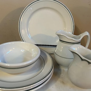 May include: A set of white ceramic dishes with a green trim. The set includes a bowl, a plate, and two pitchers.
