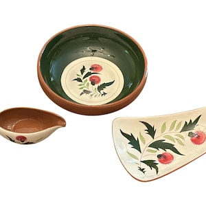 May include: A set of three ceramic serving dishes. Includes a round bowl with a green interior and floral design, a gravy boat, and a rectangular platter. All pieces feature a red, green, and white floral pattern and a terracotta rim.