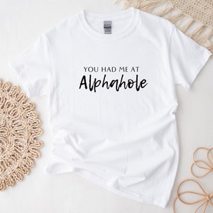 May include: White t-shirt with black text that reads "You had me at Alphahole".