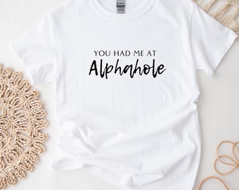 May include: White t-shirt with black text that reads "You had me at Alphahole".