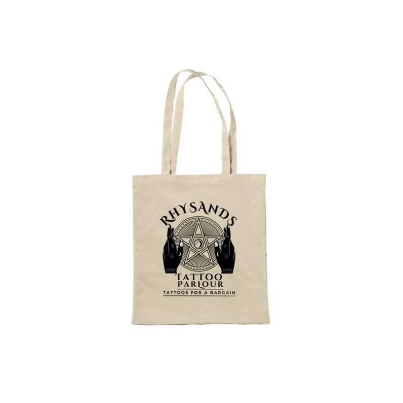 May include: A beige canvas tote bag with black text and a graphic design. The text reads "Rhysands Tattoo Parlour Tattoos for a Bargain". The graphic is a five-pointed star with a circle in the center and two hands holding the star.