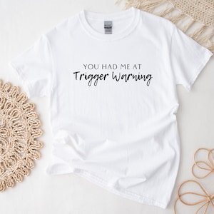 Puede incluir: Camiseta blanca con texto negro que dice "You had me at Trigger Warning."