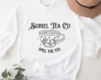 May include: White sweatshirt with black text that reads "Suriel Tea Co." and a black line drawing of a teacup with leaves and stars. The text "Spill the Tea" is below the teacup.