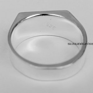 以下が含まれることがあります： 長方形のトップが付いたシルバーリングのクローズアップ。リングは滑らかで光沢があり、内側には「925」の文字が見えます。「SILVERJEWELRY2022」の文字も表示されています。