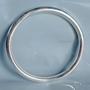 Puede incluir: Un brazalete de plata con una superficie lisa y redondeada. El brazalete está marcado con "925" en el interior.