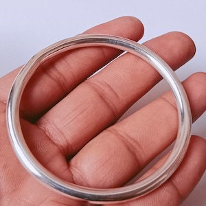 Puede incluir: Un brazalete de plata con un acabado liso y pulido.