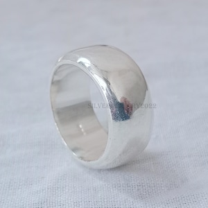 Könnte beinhalten: Ein silberner Ring mit einer abgerundeten, glatten und polierten Oberfläche. Der Ring ist dick und hat eine breite Band.