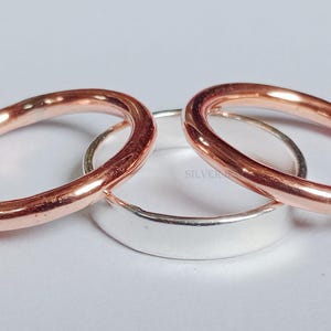 May include: Three simple metal rings, one silver and two copper, stacked on top of each other.