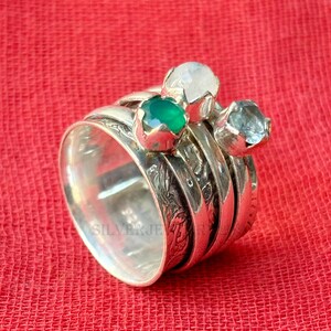 Könnte beinhalten: Ein silberner Ring mit drei Edelsteinen: einem grünen Stein, einem weißen Stein und einem blauen Stein. Der Ring ist mit einem floralen Muster graviert.