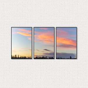 May include: A set of three framed art prints depicting a sunset sky with vivid orange and pink clouds. The bottom of each print shows silhouetted trees against a light blue sky.