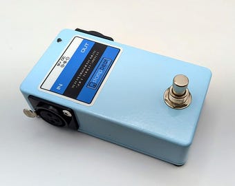 May include: A light blue stompbox with a silver switch and black input/output jacks. The box has a label with the text "stompbeat" and other text. The stompbox is rectangular and has a 9V DC input.
