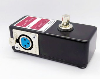 May include: Black foot pedal with a silver knob and a blue XLR connector. The pedal has a red label that says "MONO OUT" and a white label that says "XLR PLUG/TO MUTE IN".