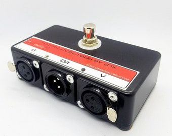 May include: Black XLR audio switcher box with three female XLR connectors, a red label that says "PHANTOM POWERED 15V/105", and a black foot switch with a silver knob. The label also says "XLR 48V PERMANENT SWITCH".
