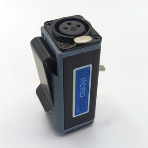 May include: A rectangular black and grey audio device featuring a top-mounted XLR input port with a silver push release button. The side displays a blue label with the white text stompbeat.com and a black metal belt clip is attached to the side.