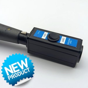 Puede incluir: Un interruptor XLR negro con etiquetas azules y texto blanco que dice "ON" y "OFF". El interruptor tiene un botón negro y está conectado a un componente cilíndrico negro. Una pegatina azul de "NUEVO PRODUCTO" está en la esquina inferior izquierda.