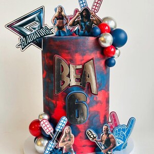 Peut inclure: Un gâteau décoré avec un glaçage rouge et bleu, portant le nom "BEA" et le chiffre "6". Le gâteau est orné d'images comestibles de lutteurs, de ballons et du mot "GLADIATORS".