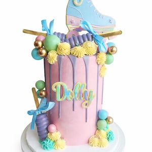May include: A pink birthday cake decorated with a light blue ice skate topper, colourful candies, and the name "Dolly". The cake has purple frosting drips and is decorated with yellow and blue frosting swirls.
