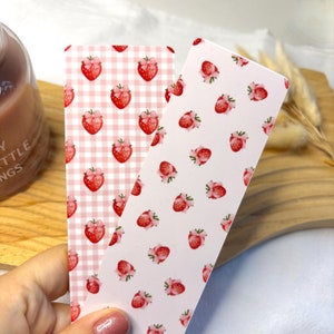 May include: Two pink and white gingham bookmark designs with a strawberry pattern. One bookmark has a white background with pink gingham squares and the other has a pink background with white gingham squares.
