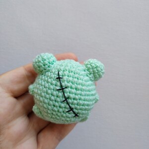 May include: A small, green crocheted plush toy shaped like a monster with black stitches across its body.