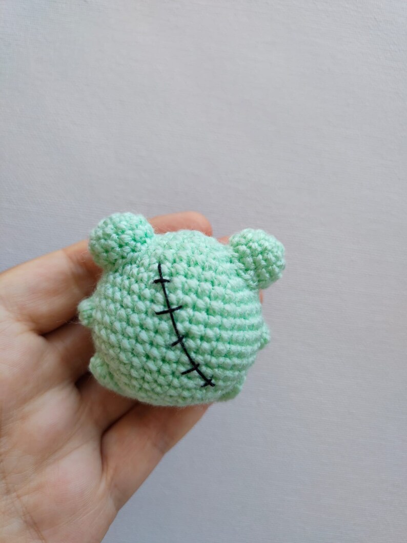 May include: A small, green crocheted plush toy shaped like a monster with black stitches across its body.