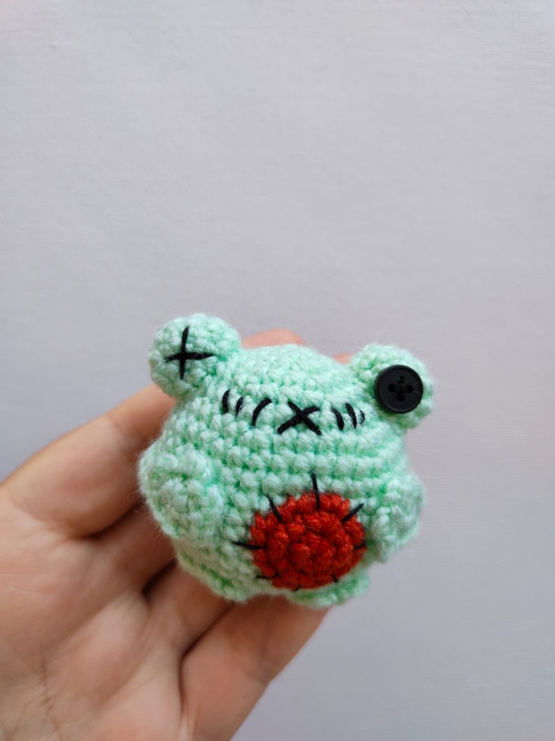 May include: A small green crocheted frog with a red heart on its belly and a black button for an eye.