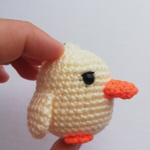 May include: A crocheted yellow chick with orange beak and feet. The chick has a black eye and is made of a soft, textured yarn. The handmade chick is a small, round shape.