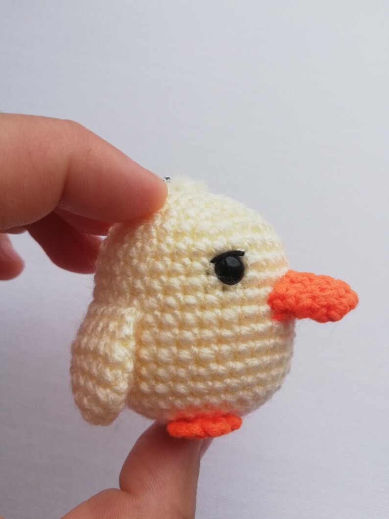 May include: A crocheted yellow chick with orange beak and feet. The chick has a black eye and is made of a soft, textured yarn. The handmade chick is a small, round shape.