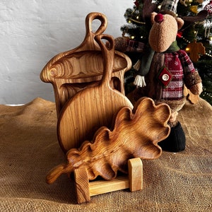 May include: Three wooden serving boards in the shape of an acorn, a circle, and an oak leaf. The boards are stacked on a wooden stand.