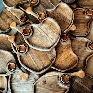 Op de afbeelding: Een stapel houten serveerschalen in de vorm van een kippenpoot. De schalen hebben een kleine inkeping voor een dip of saus. De schalen zijn gemaakt van donker hout en hebben een natuurlijke afwerking.