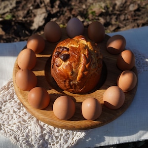May include: A wooden serving platter displays a baked bread and a circle of brown eggs. The bread is golden brown with a dark, textured top. The eggs are a mix of light and medium brown, arranged around the bread on the wooden platter.