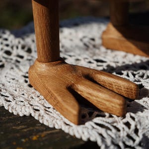May include: Close-up of a wooden object with a fork-like base. The object is made of light brown wood and sits on a white, crocheted surface. The wooden base has three prongs, and the wood grain is visible.