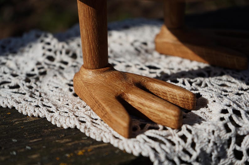 May include: Close-up of a wooden object with a fork-like base. The object is made of light brown wood and sits on a white, crocheted surface. The wooden base has three prongs, and the wood grain is visible.