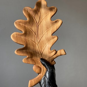 May include: A wooden oak leaf serving tray with a carved acorn detail. The tray is made of natural wood and has a rustic, organic look.