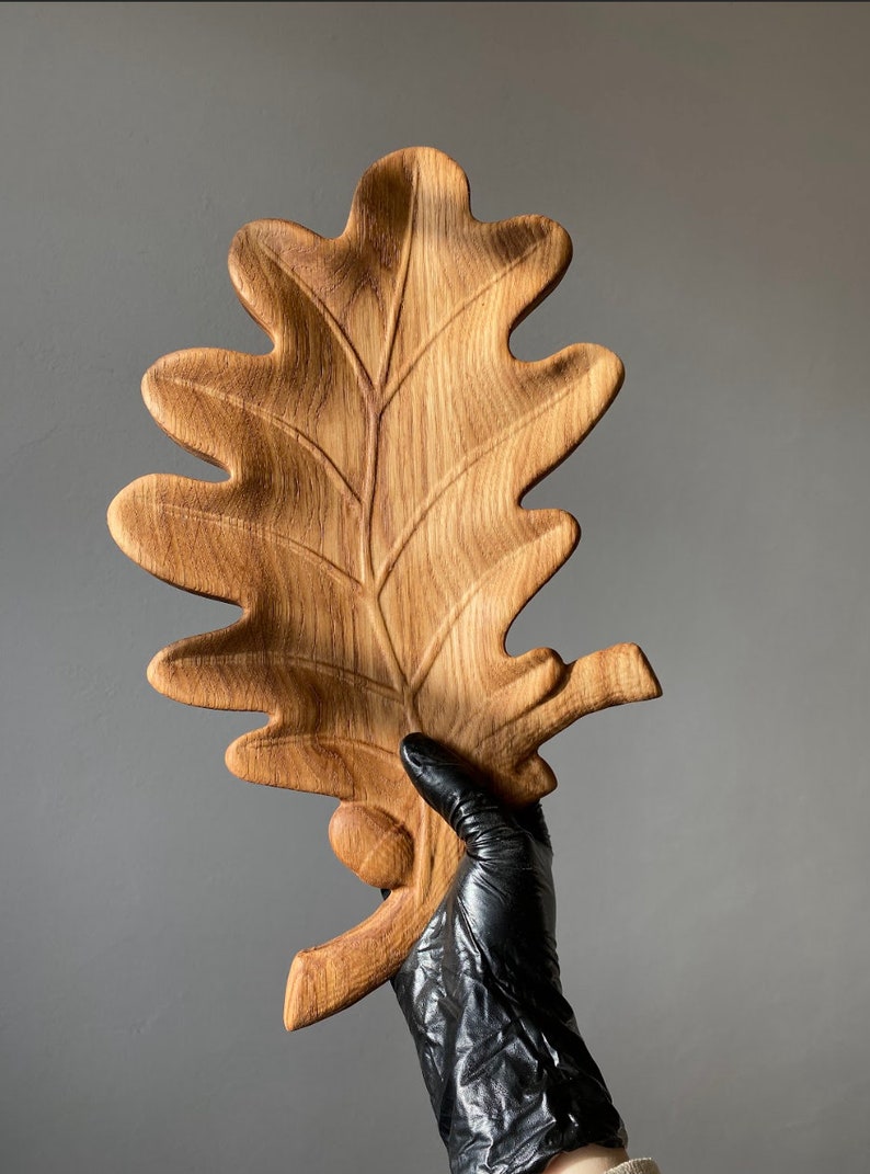 May include: A wooden oak leaf serving tray with a carved acorn detail. The tray is made of natural wood and has a rustic, organic look.