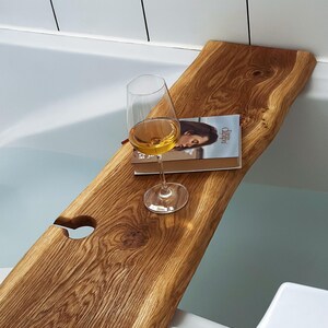 Könnte beinhalten: Ein Holz-Badetablett mit einer Aussparung für ein Weinglas und ein Buch. Das Tablett befindet sich in einer mit Wasser gefüllten Badewanne.