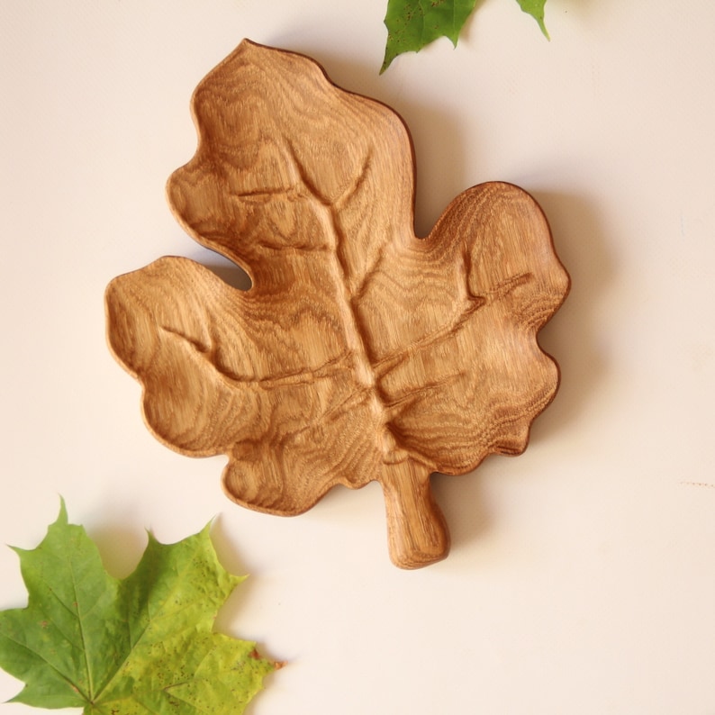 May include: A wooden leaf-shaped serving tray made of oak wood. The tray has a natural wood finish and is carved to resemble a leaf.