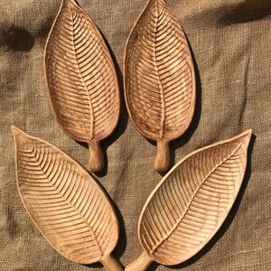 May include: Four wooden leaf-shaped serving trays with a natural wood finish. The trays are arranged in a circle on a brown burlap background.