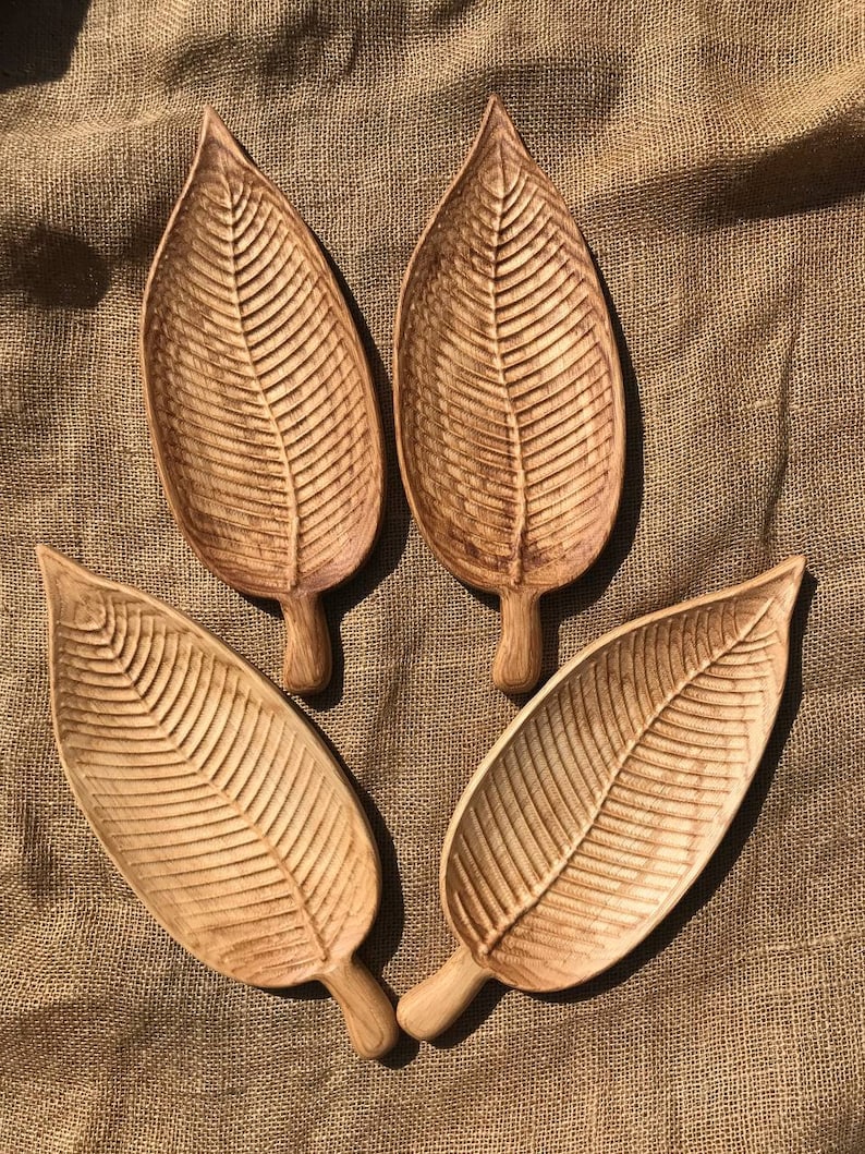 May include: Four wooden leaf-shaped serving trays with a natural wood finish. The trays are arranged in a circle on a brown burlap background.
