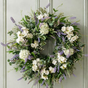 Peut inclure: Une couronne circulaire ornée de fleurs blanches, de brins de lavande et de feuillage vert. La couronne est composée de diverses textures et nuances de vert, de blanc et de violet, créant une esthétique naturelle et accueillante. Idéale pour l'intérieur ou l'extérieur.