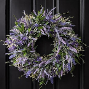 May include: A circular wreath composed of lavender-colored flowers and green foliage. The wreath is densely packed with various textures and shades of purple and green, creating a natural and inviting aesthetic. The wreath is displayed against a black background.