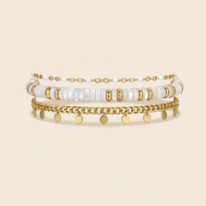 May include: A stack of three bracelets. The top bracelet is a delicate gold chain with small white beads. The middle bracelet features white, rectangular beads with gold accents. The bottom bracelet is a gold chain with small, dangling gold discs.