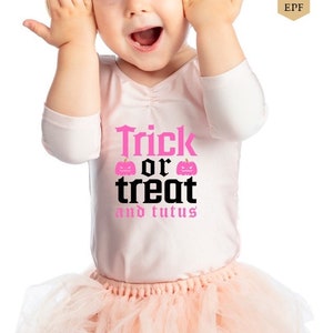 May include: A young child wearing a pink tutu and a white shirt with the text "Trick or treat and tutus" in black and pink. The child is smiling and has their hands on their cheeks.