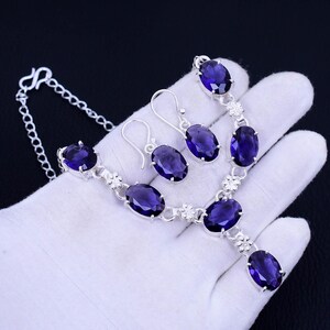 May include: A silver necklace and earrings set with oval-shaped amethyst gemstones. The necklace has a delicate chain and a pendant with a larger amethyst stone. The earrings are simple and elegant, with a single amethyst stone.