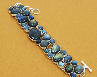 May include: A silver bracelet featuring a series of oval and round labradorite stones in shades of blue, gray, and green. The stones are set in a silver metal setting and connected by silver links. The bracelet has a toggle clasp.