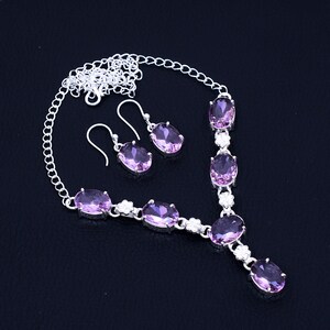 May include: A silver necklace and earrings set with oval-shaped pink gemstones. The necklace features a delicate chain with a pendant and multiple gemstones.