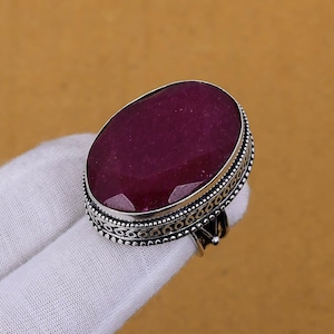 May include: A silver ring with an oval-shaped, deep red gemstone set in a silver bezel. The ring has a decorative, ornate silver band.